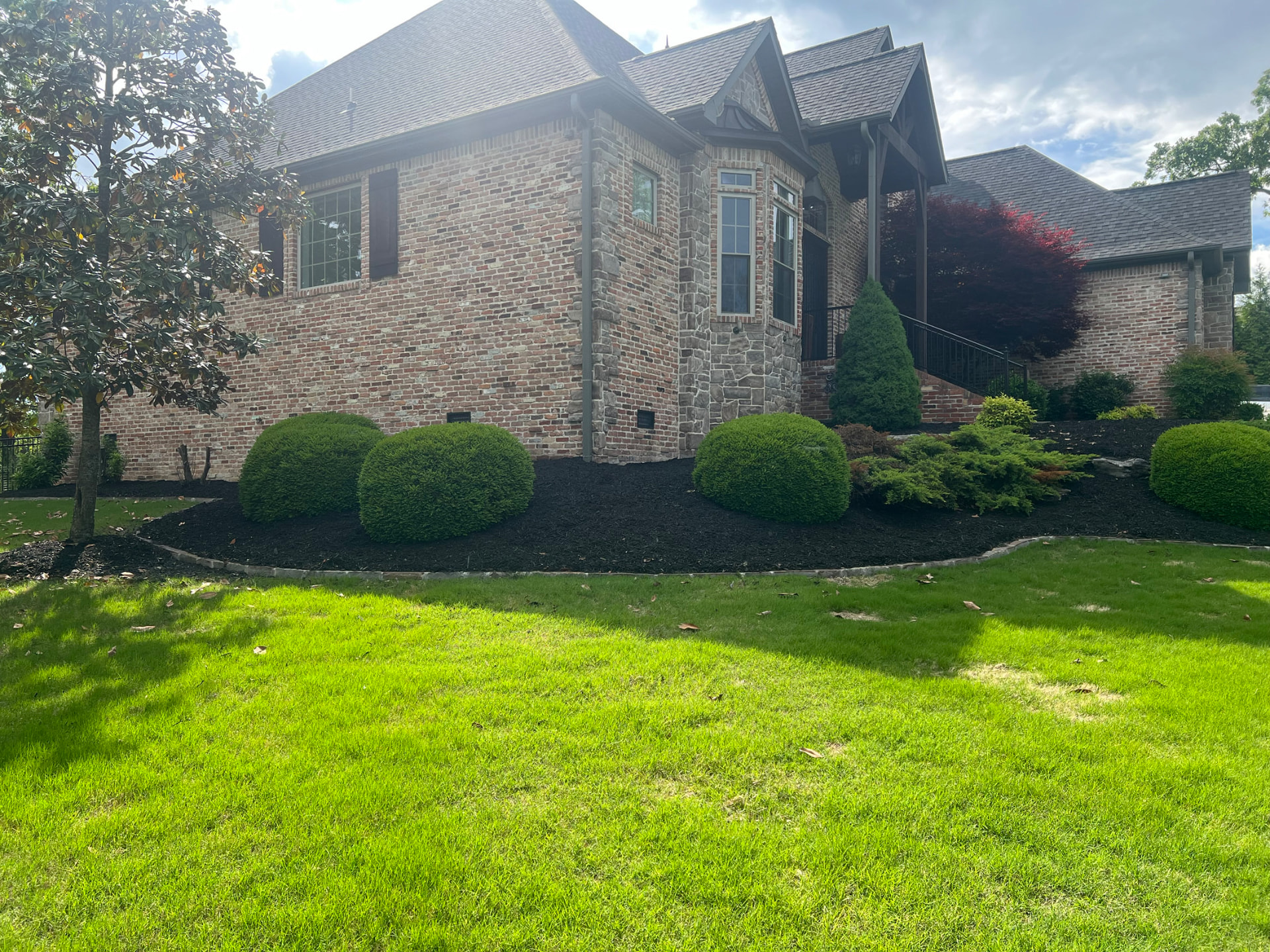Freshly cut green lawn with neatly edged, mulched shrub beds in front of a brick home